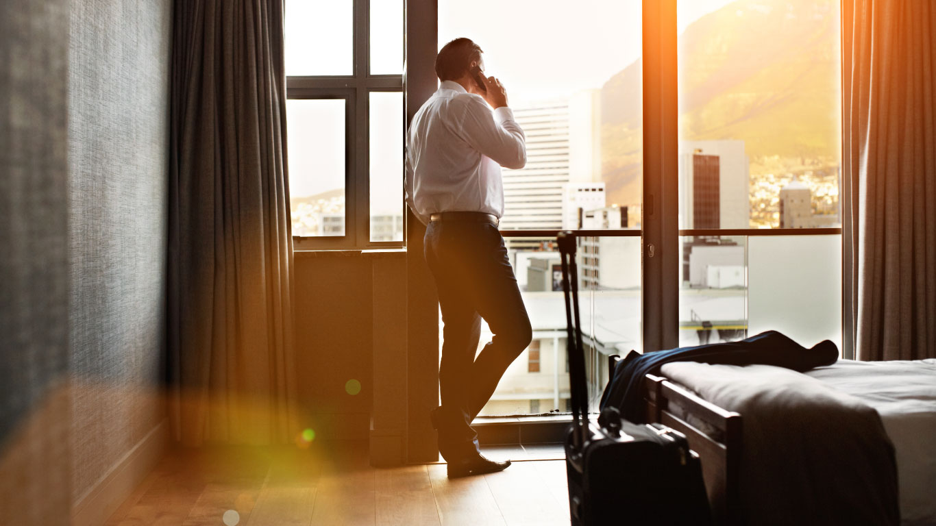 Hotel guest standing by the window on a phone call taking a look at the view outside of his window
