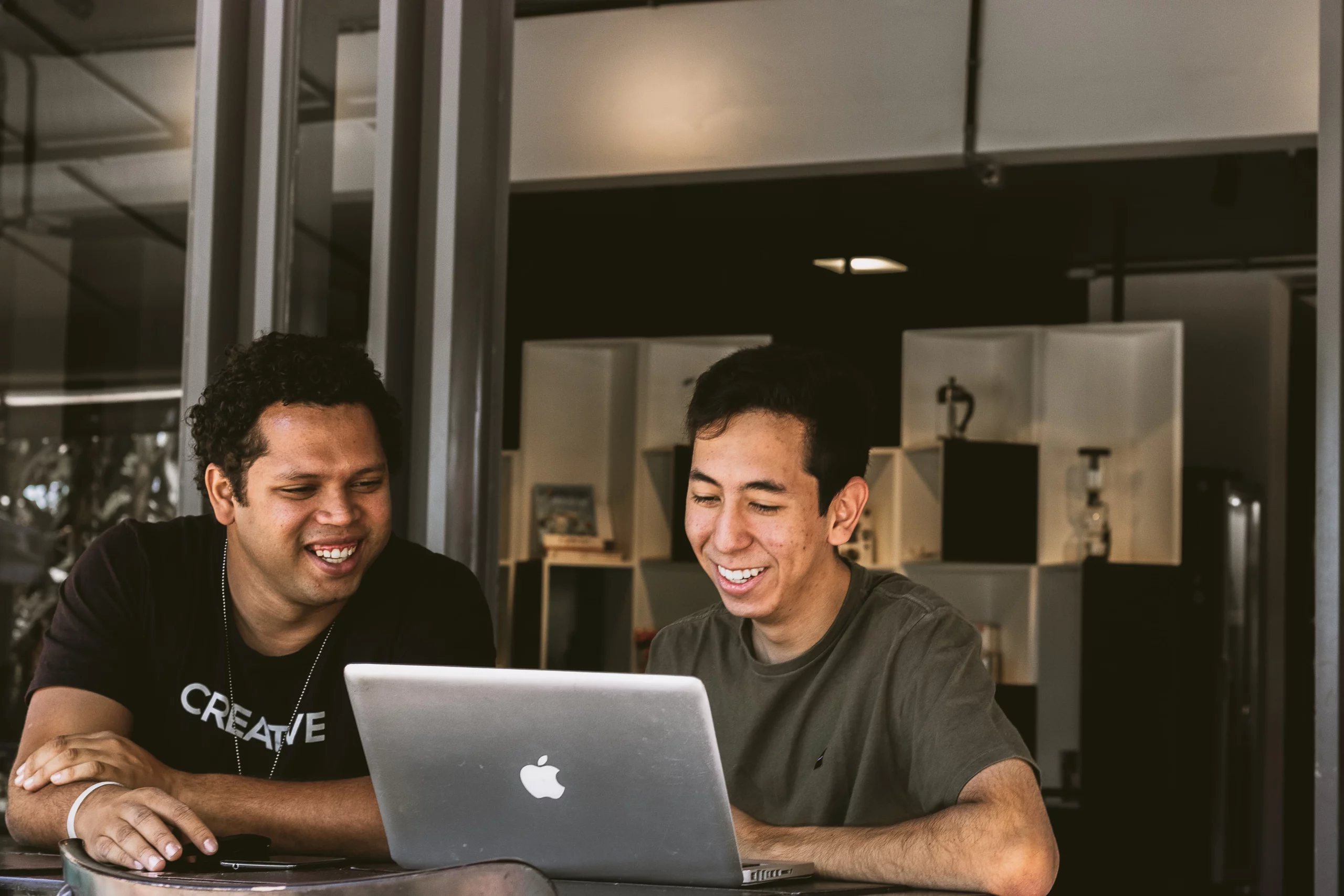 two men working on a laptop together and smiling.