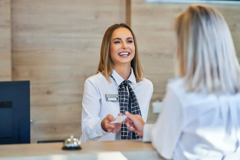 Hotel front desk smiling at a customer and handing her a key