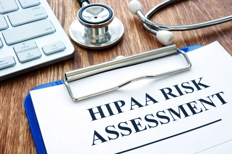 desk and clipboard with a sheet of paper that reads, "HIPAA Risk Assessment" - meant to showcase a checklist for maintaining records of compliance.